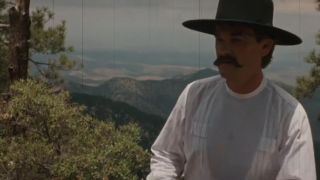 Kurt Russell wearing a black hat with a vista of mountains behind him