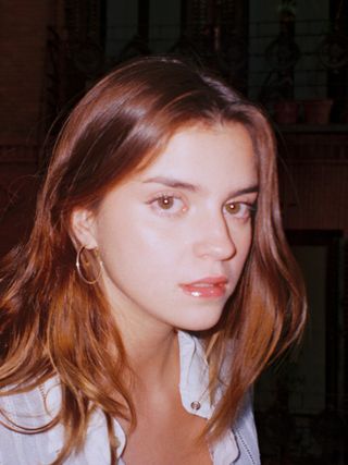 Portrait of actress Carla Tous wearing a white button-down shirt and thin gold hoop earrings.