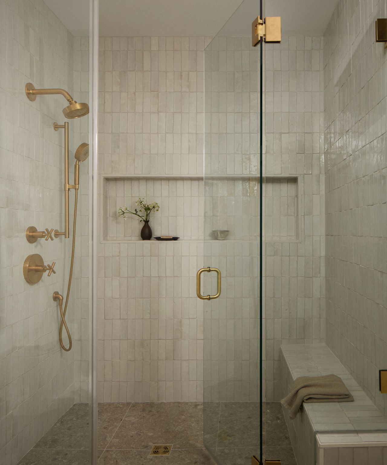 A walk-in shower with zellige tile and gold fixtures