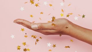A hand with pixie dust nails on a pink backdrop