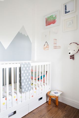 Scandi-style child's bedroom with white cot, white walls, brown floorboards and mountain-effect pattern on walls with grey paint