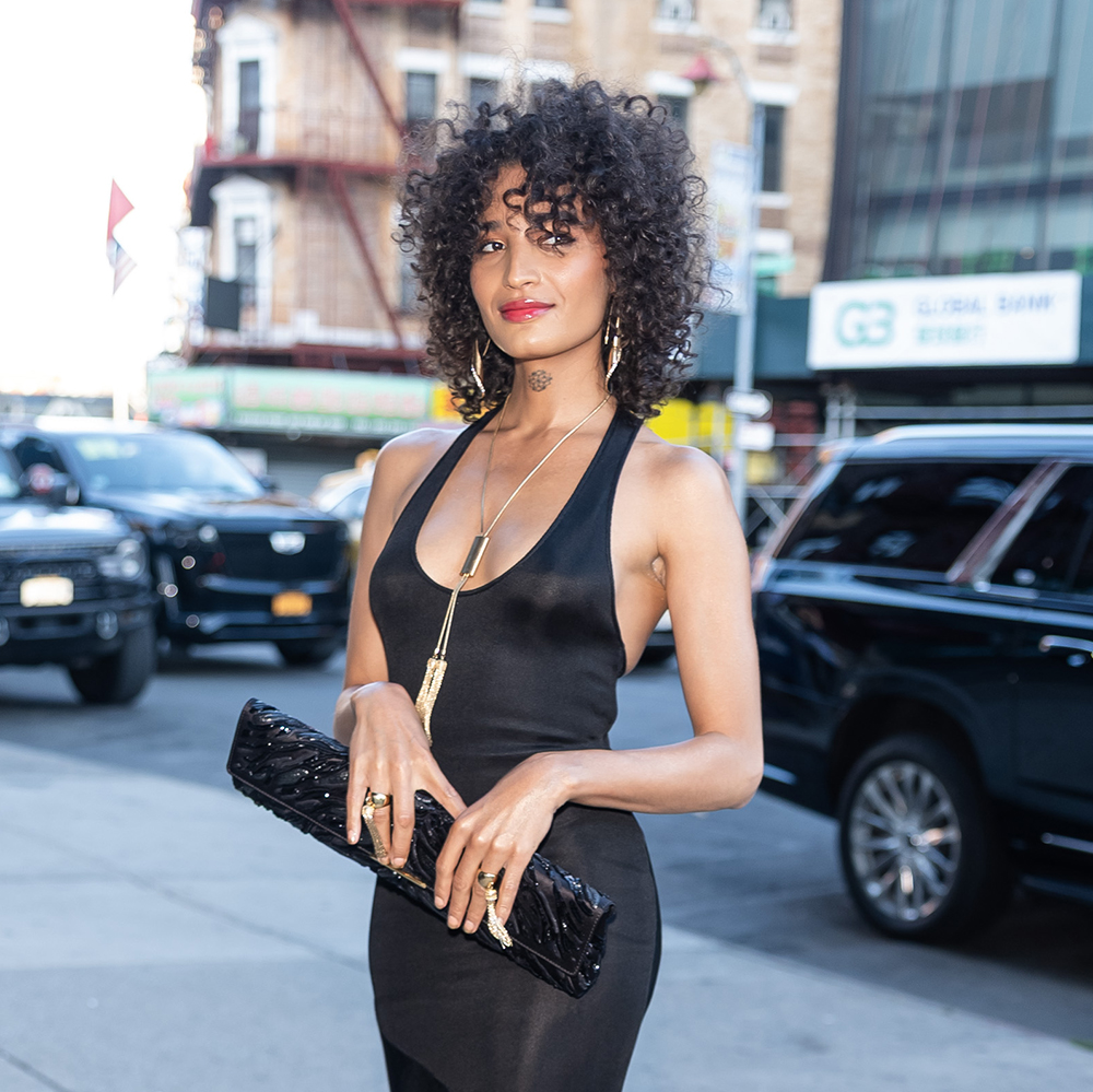 Indya Moore wearing a black long dress with violet pointed toe heels 