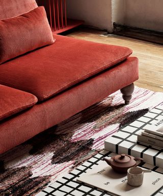 Close up of red sofa, patterned rug underneath, checkered style coffee table with magazines and ornaments