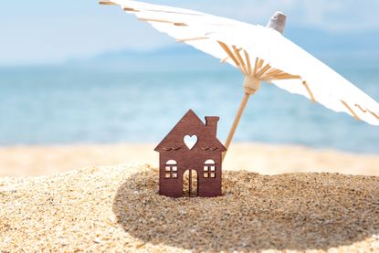 A mini home under a small parasol on a sunny beach, with the sea in the background