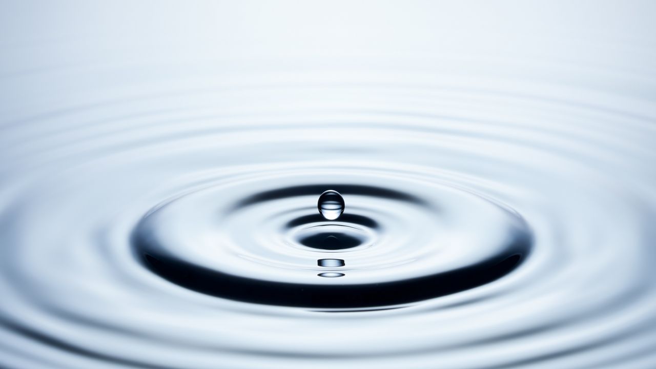 A drop of water suspended above ripples.