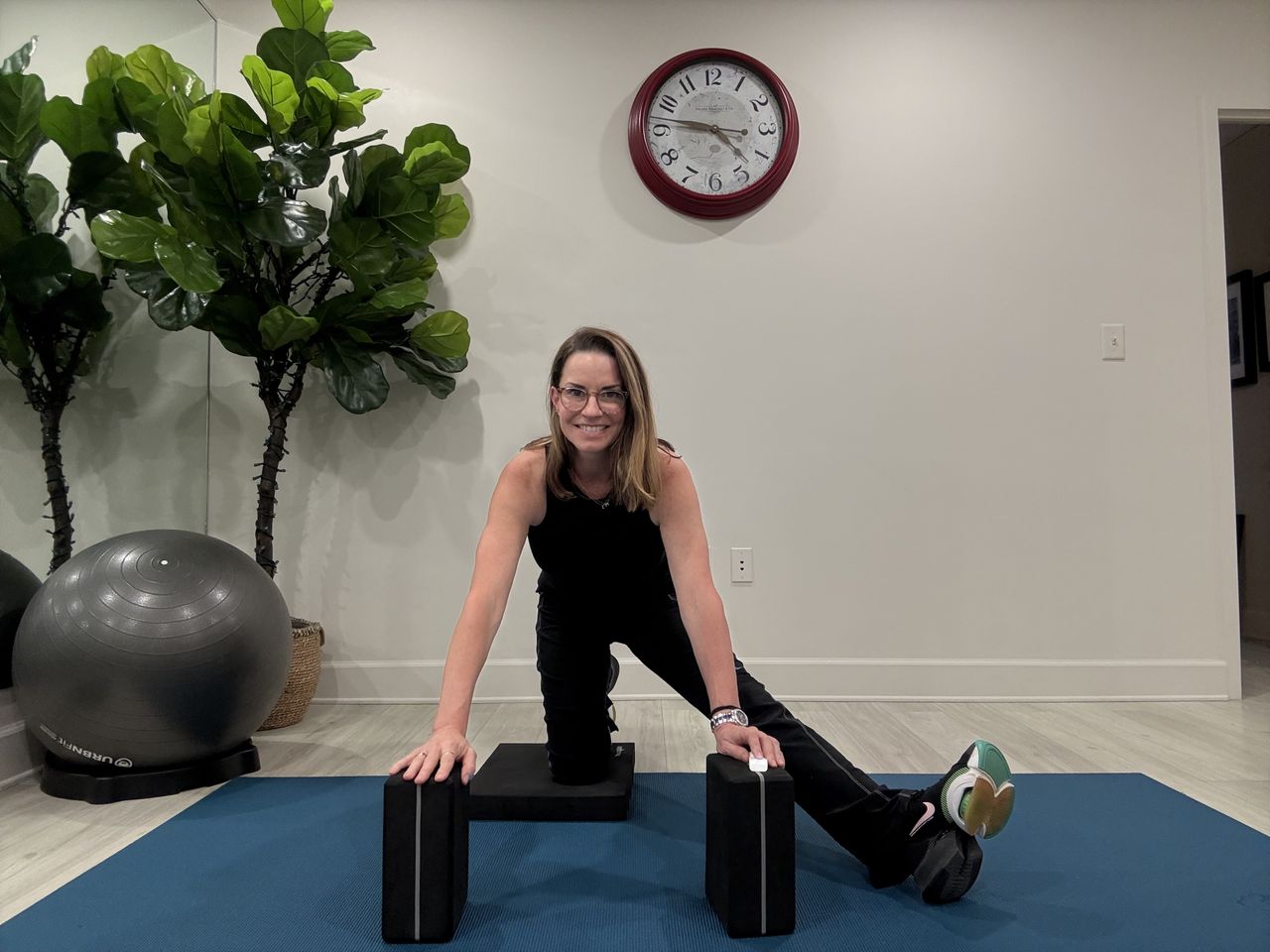 An employee at Femina physical therapy performs a kneeling lunge. Her front leg is positioned out to the side and held straight as she pushes her hips back.