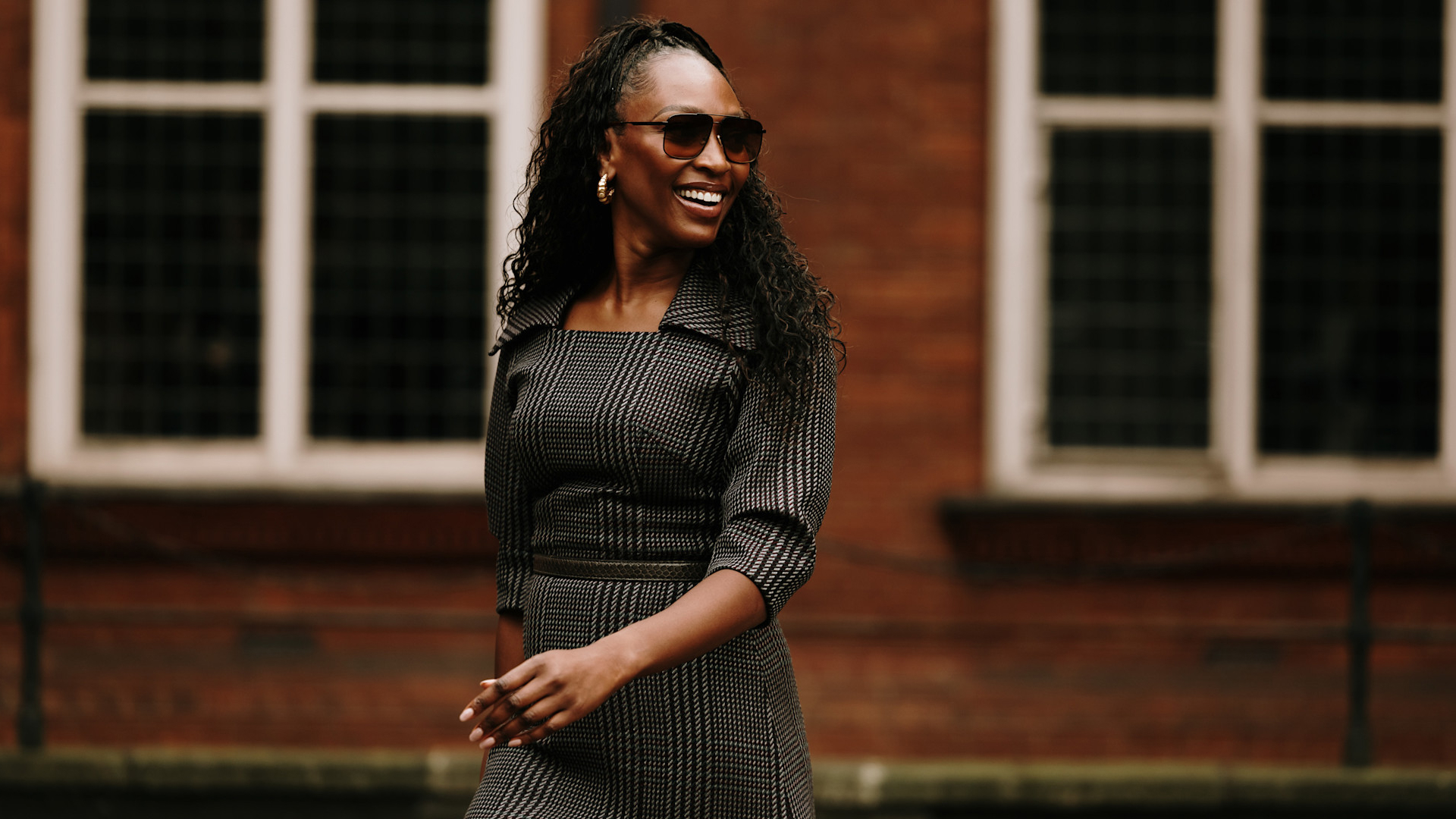 a london spring 2025 fashion week attendee smiling and wearing a checkered dress and sunglasses