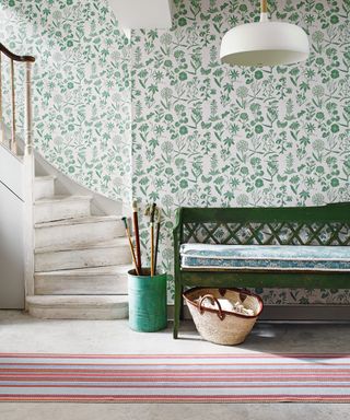 Small hallway ideas shown with green floral wallpaper, a red striped rug and green bench.