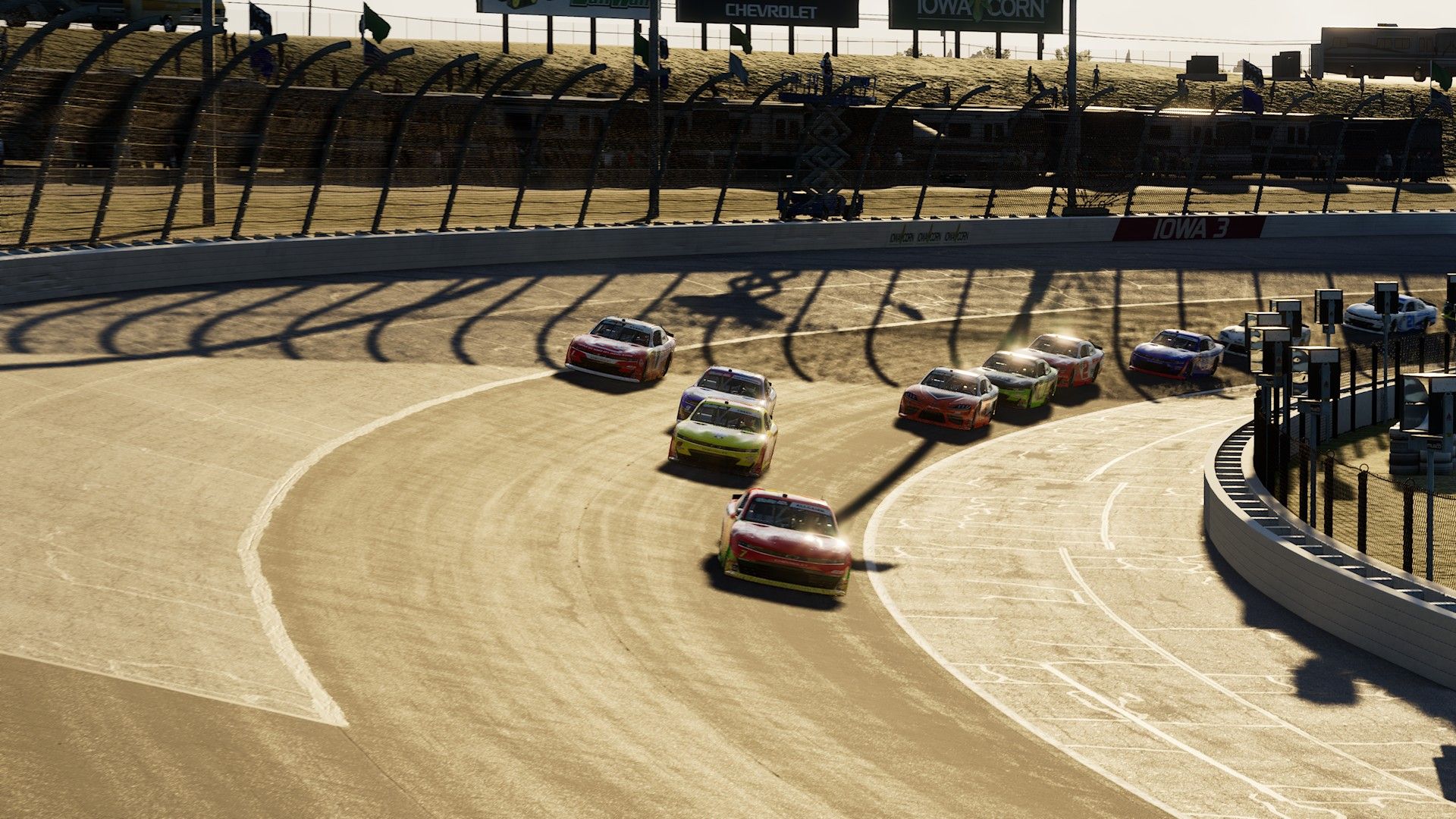 A screenshot from NASCAR 26 showing O'Reilly Series cars racing under a low sun at Iowa Speedway.