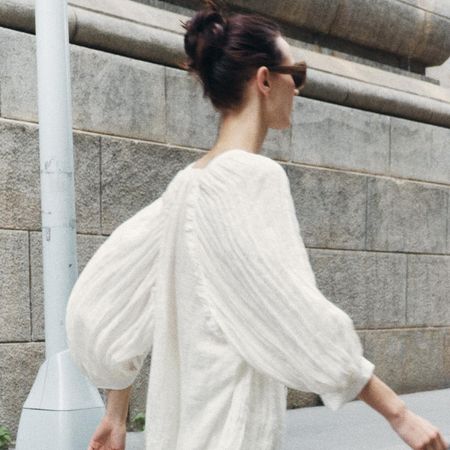 Zara model wearing an off-white wrinkled satin blouse with matching trousers and sunglasses.