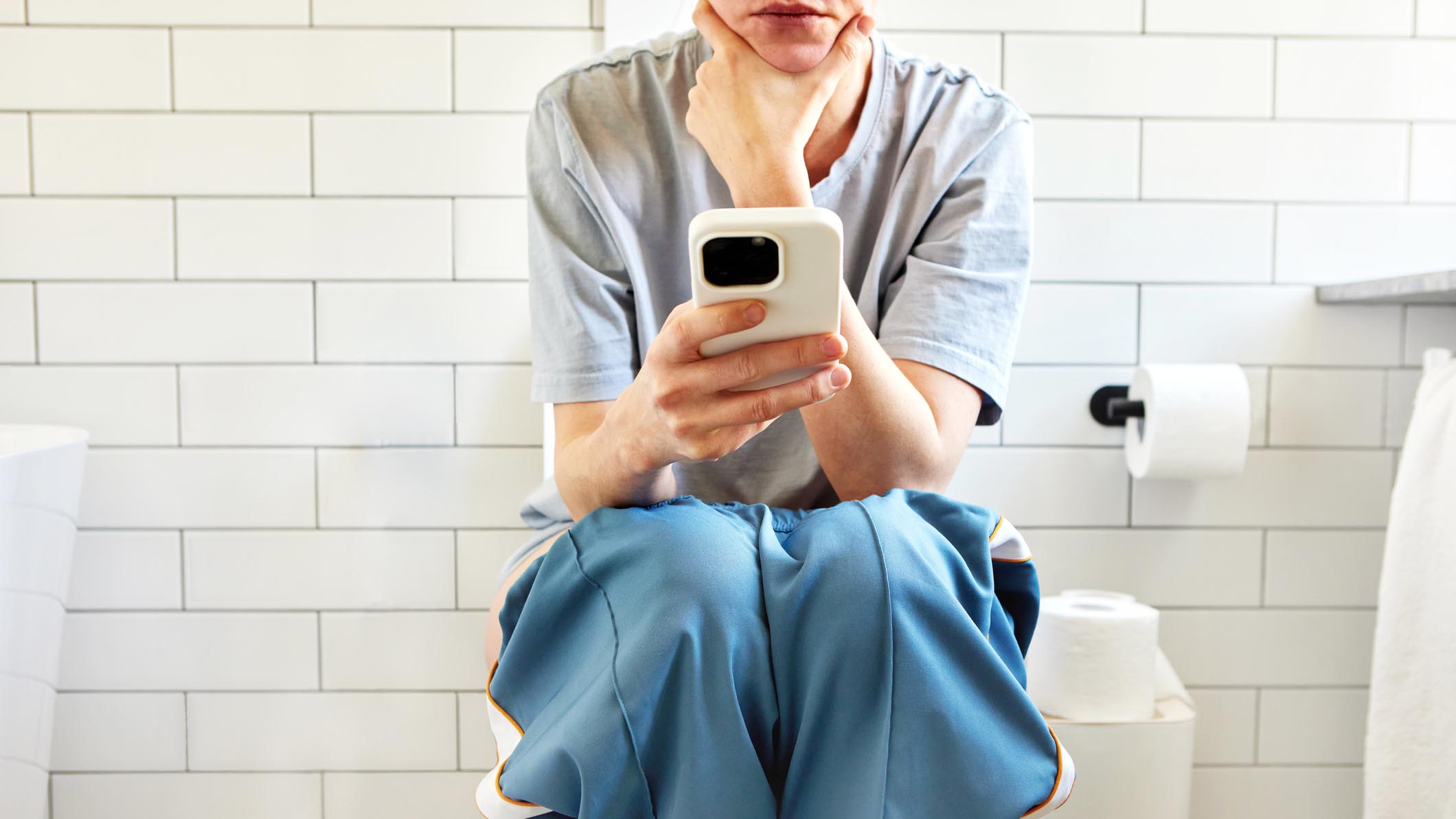 a woman sat on her smart phone on the toilet 