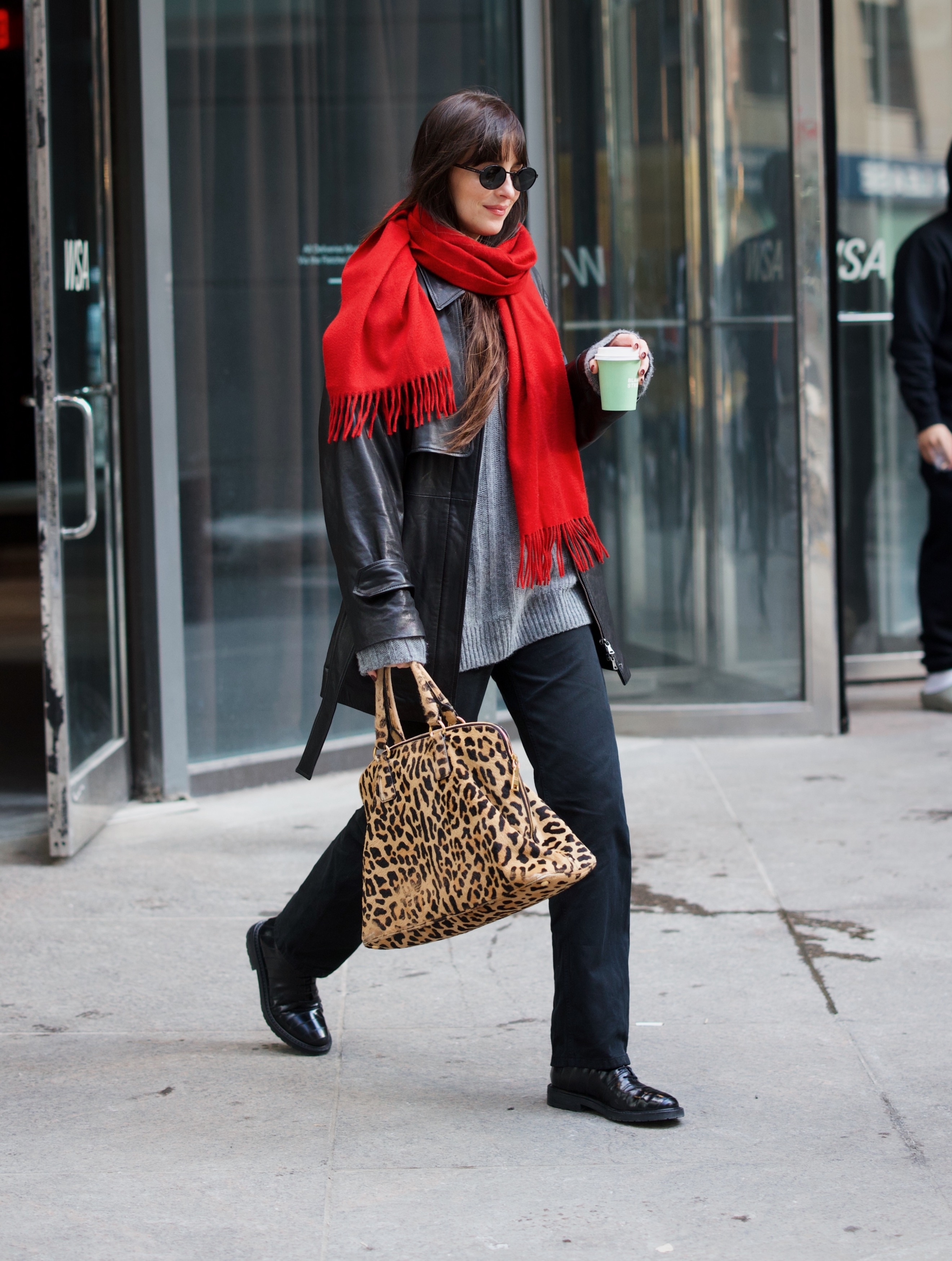 Dakota Johnson wears a red scarf, grey jumper, black leather jacket, black jeans, black boots