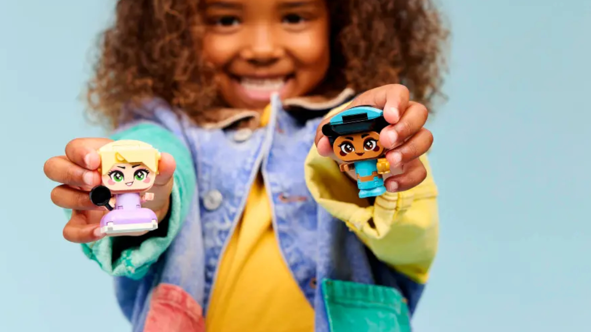 A smiling child holds out Mini Jasmine and Rapunzel figures