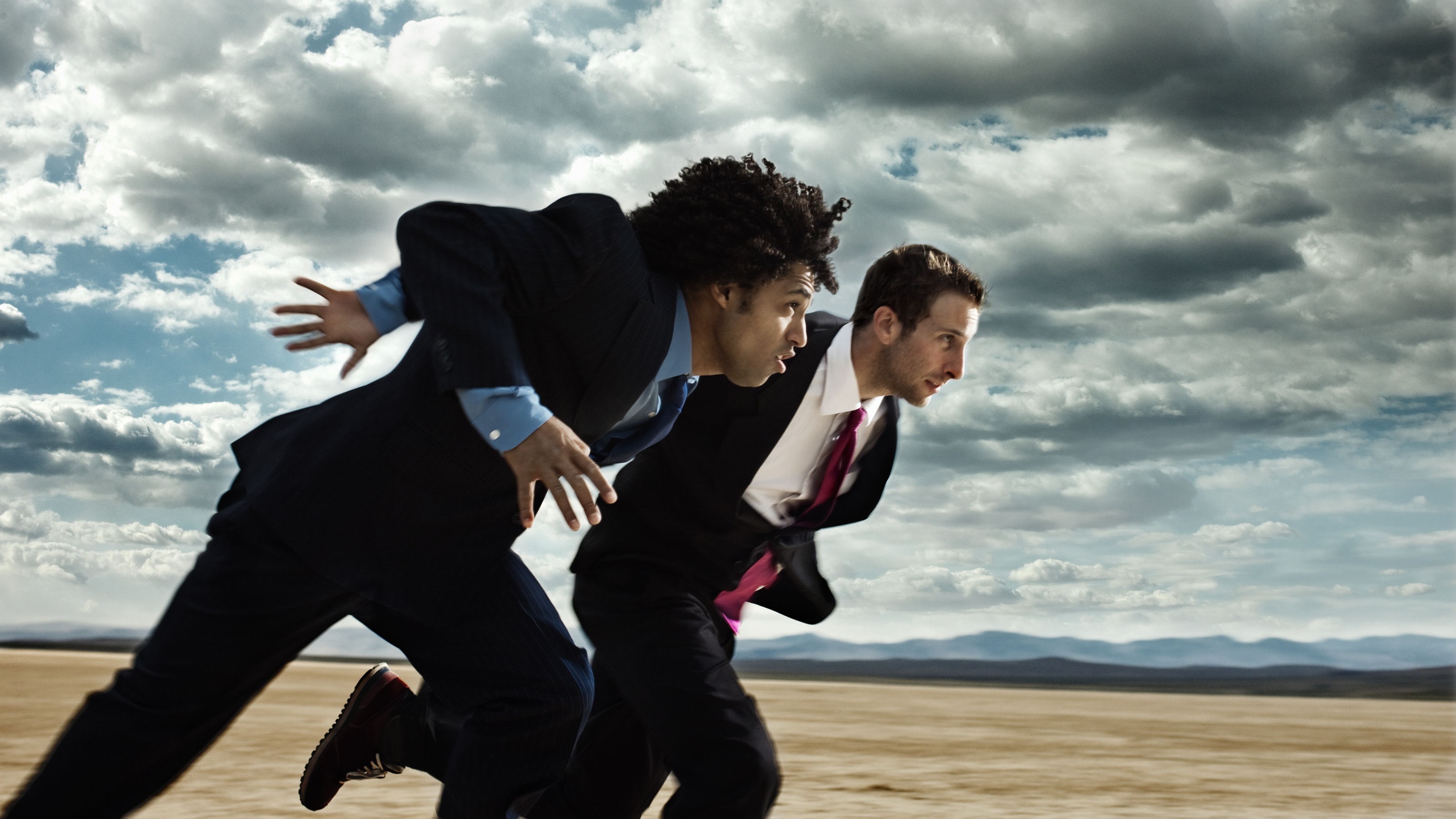 Two business executives in suits compete in a footrace in the dessert.