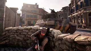 Sniper Elite Resistance review; a man hides behind sand bags as a tank goes past