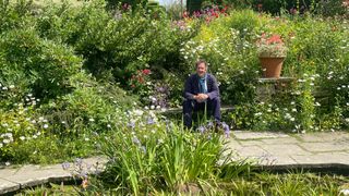 Monty sitting by a large pond surrounded by wildflowers