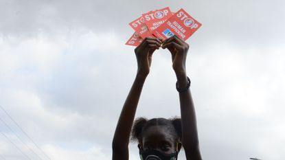 A little girl demonstrating in a face mask in Nigeria lifts 'stop human trafficking' leaflets