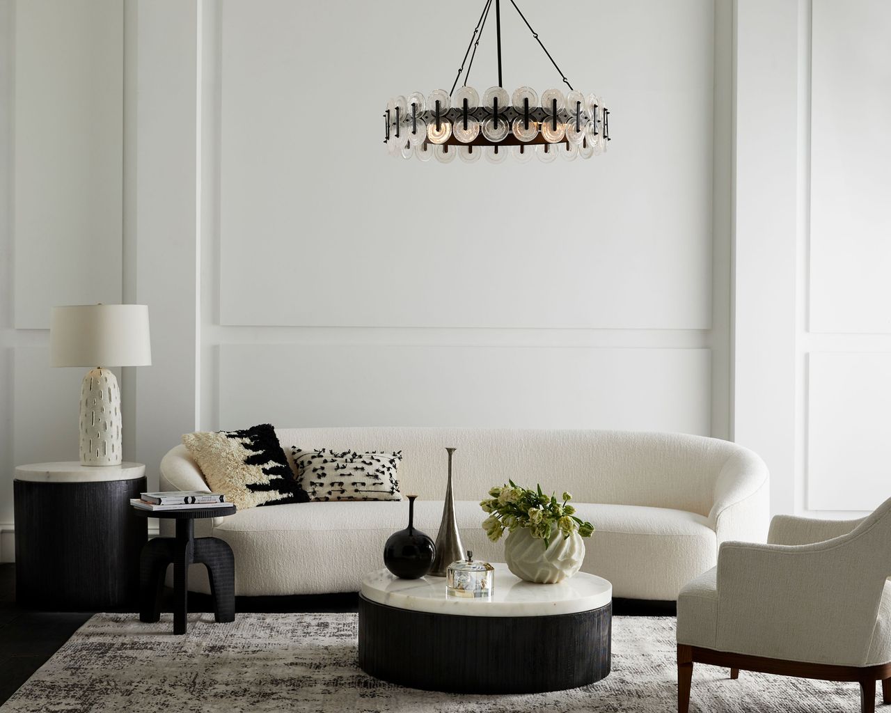 A whiteliving room with white sofa, black coffee table and black chandelier