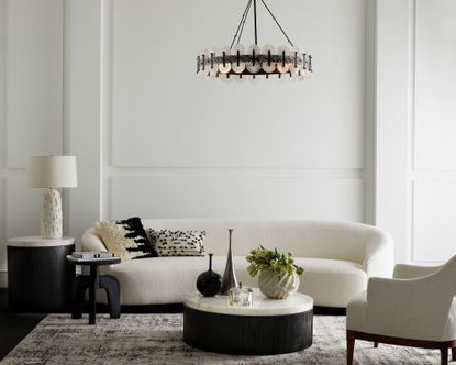 A whiteliving room with white sofa, black coffee table and black chandelier
