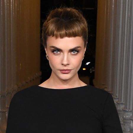 Cara Delevigne with an updo hairstyle that has bangs. She's also wearing a black dress. 
