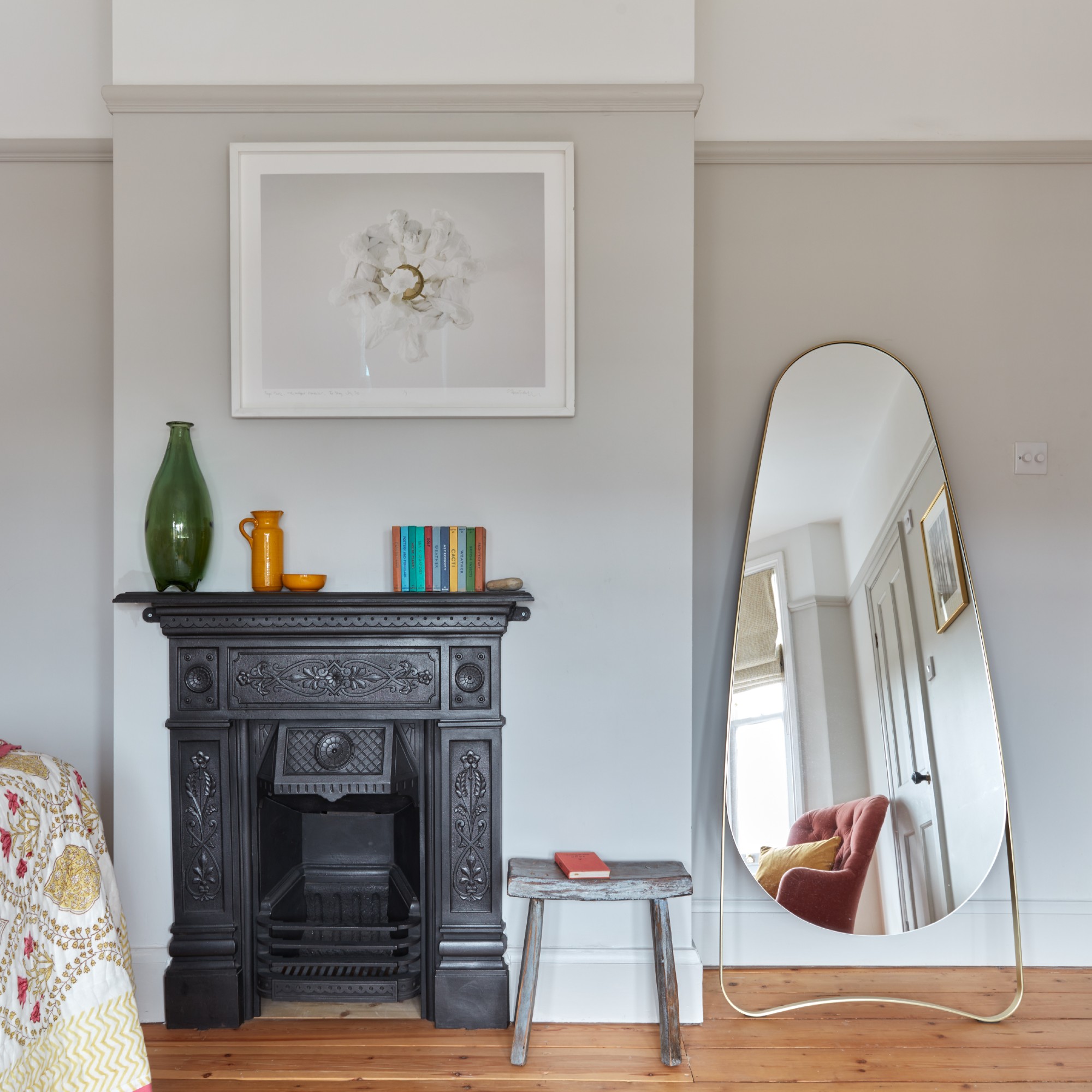 A light grey-painted bedroom with a black fireplace and a curved chrome full-length mirror