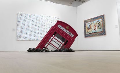 A submerged red telephone booth is set on the gallery room floor.