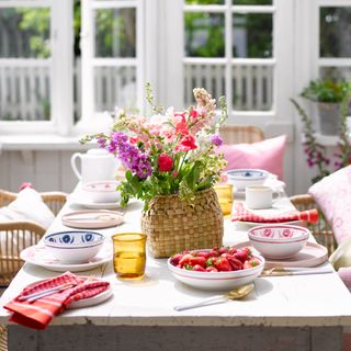 Daytime dining in white conservatory with table decorated with dinnerware and strawberries