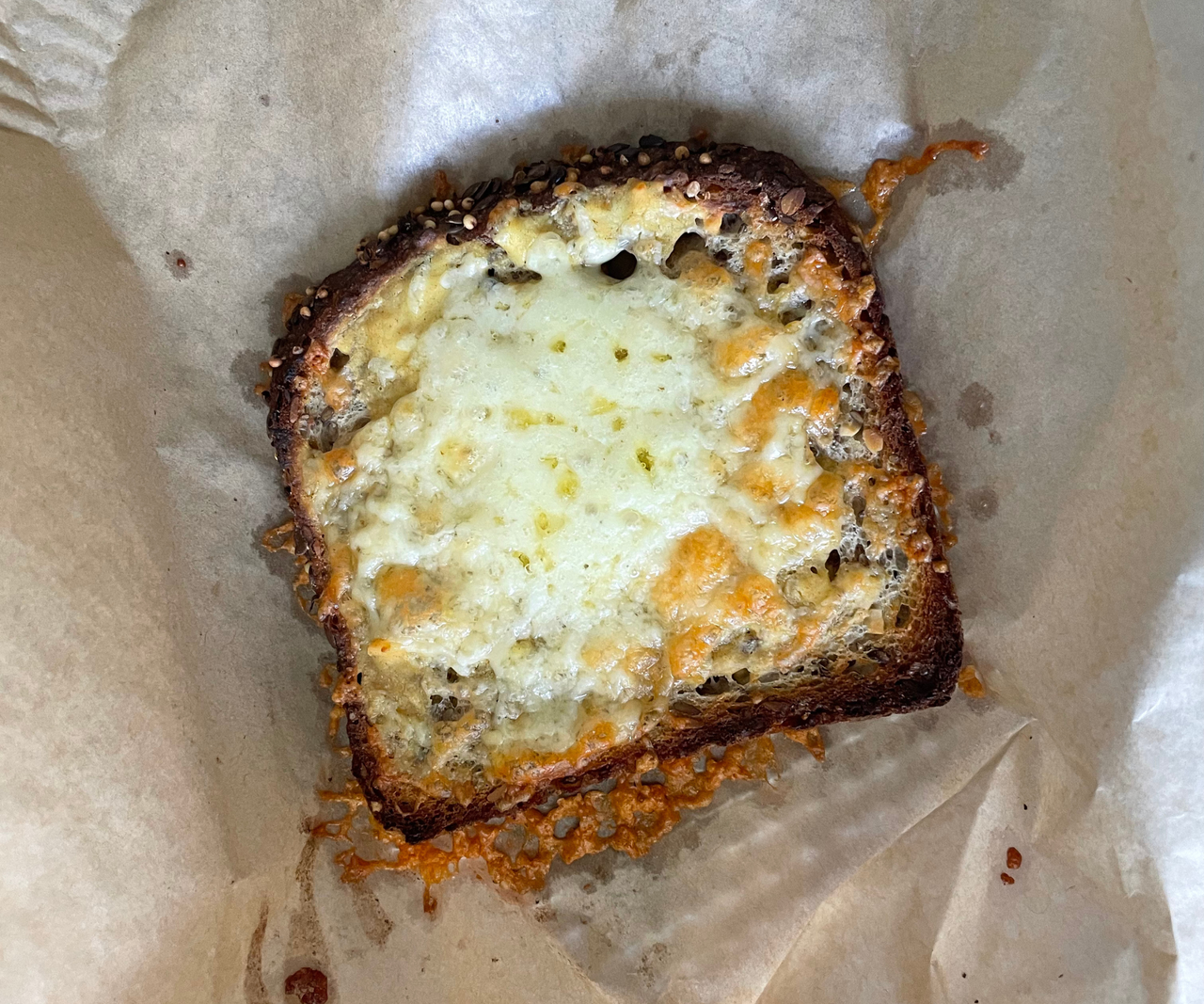 A toasted piece of bread with melted cheese on top, one a piece of unbleached parchment paper.