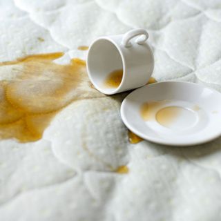 A cup of coffee spilled out over the top of a mattress