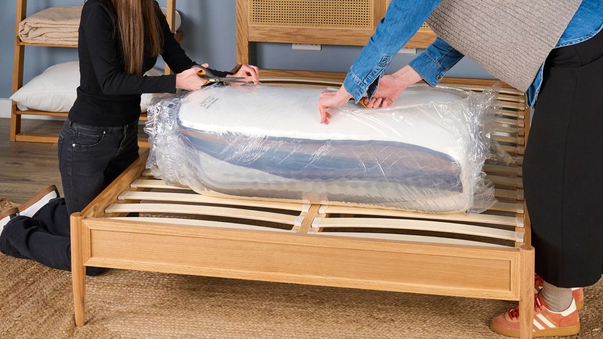 Testers use scissors to cut the plastic wrapping of an unboxed Brooklyn Bedding CopperFlex Pro hybrid mattress.