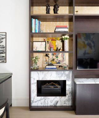 Living room detail with brown bookcase and integrated gas fireplace with marble surround