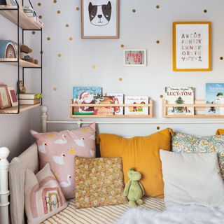 Children's room with day bed with cushions and bookshelf on wall.