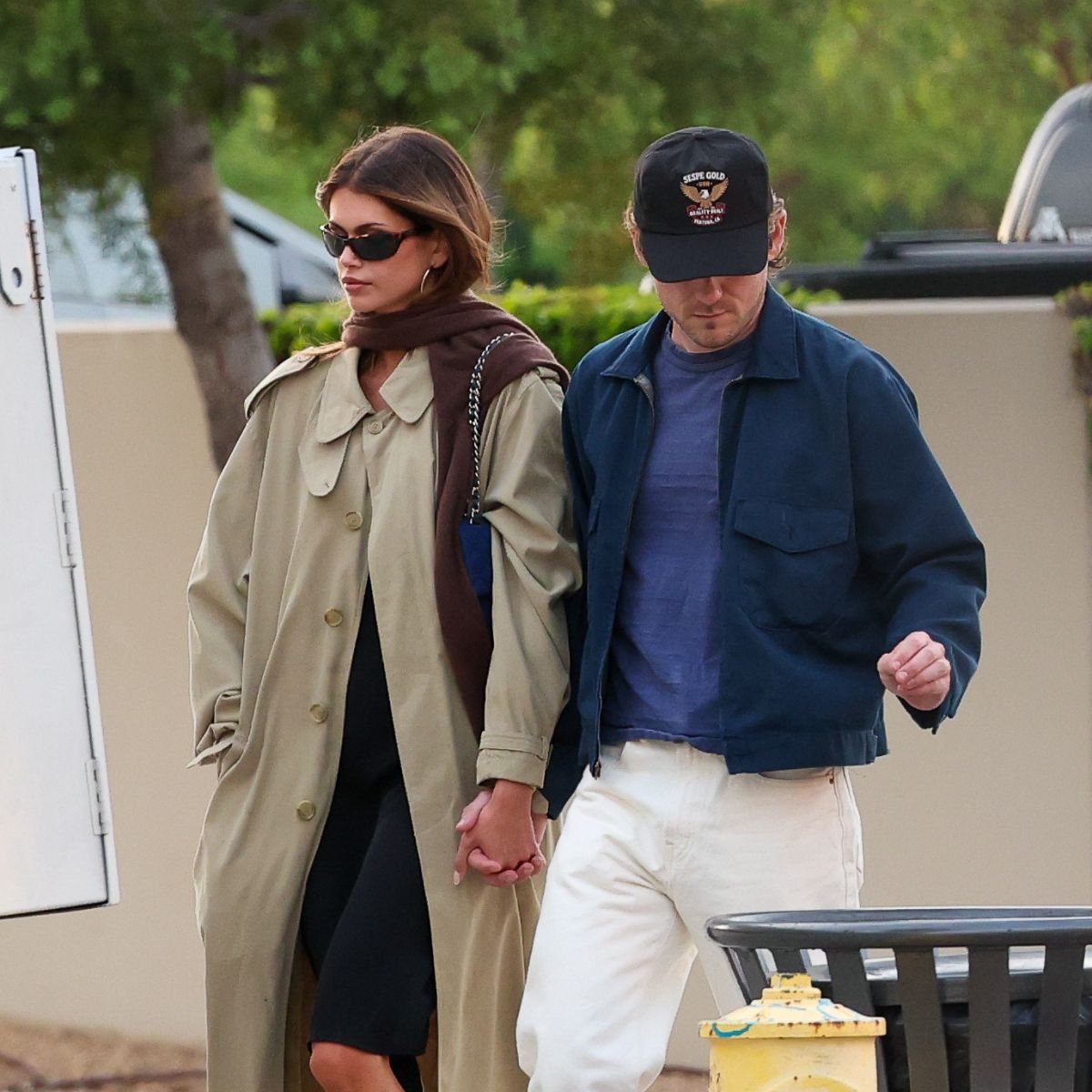 An image of Kaia Gerber wearing a trench coat with a black dress and ballet flats.