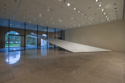 The lobby at the Rice Gallery. Beige tiles with white walls, with concrete arches at the front of the building seen through the glass entry.