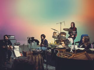 En promobild för The Beatles Get Back där hela gänget sitter och spelar vid sin musikutrustning mot en färgglad bakgrund
