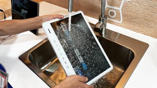 Sylvox Portable TV is held under a running tap, with water flowing down the screen