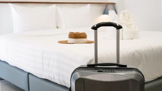 A suitcase in front of a mattress in a hotel room