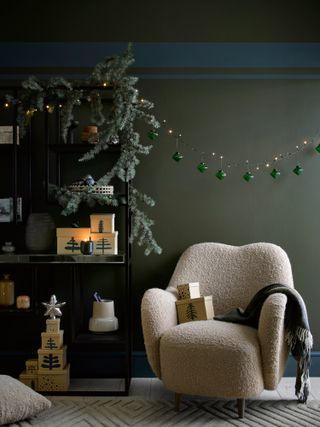 Green living room with bookshelves draped with pine garland, string of fairy lights with green glass baubles suspended off them