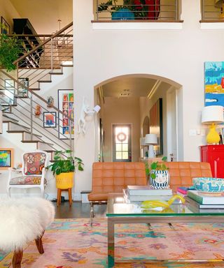 open-plan living room with neutral walls, open staircase, tan leather chairs and colorful artwork