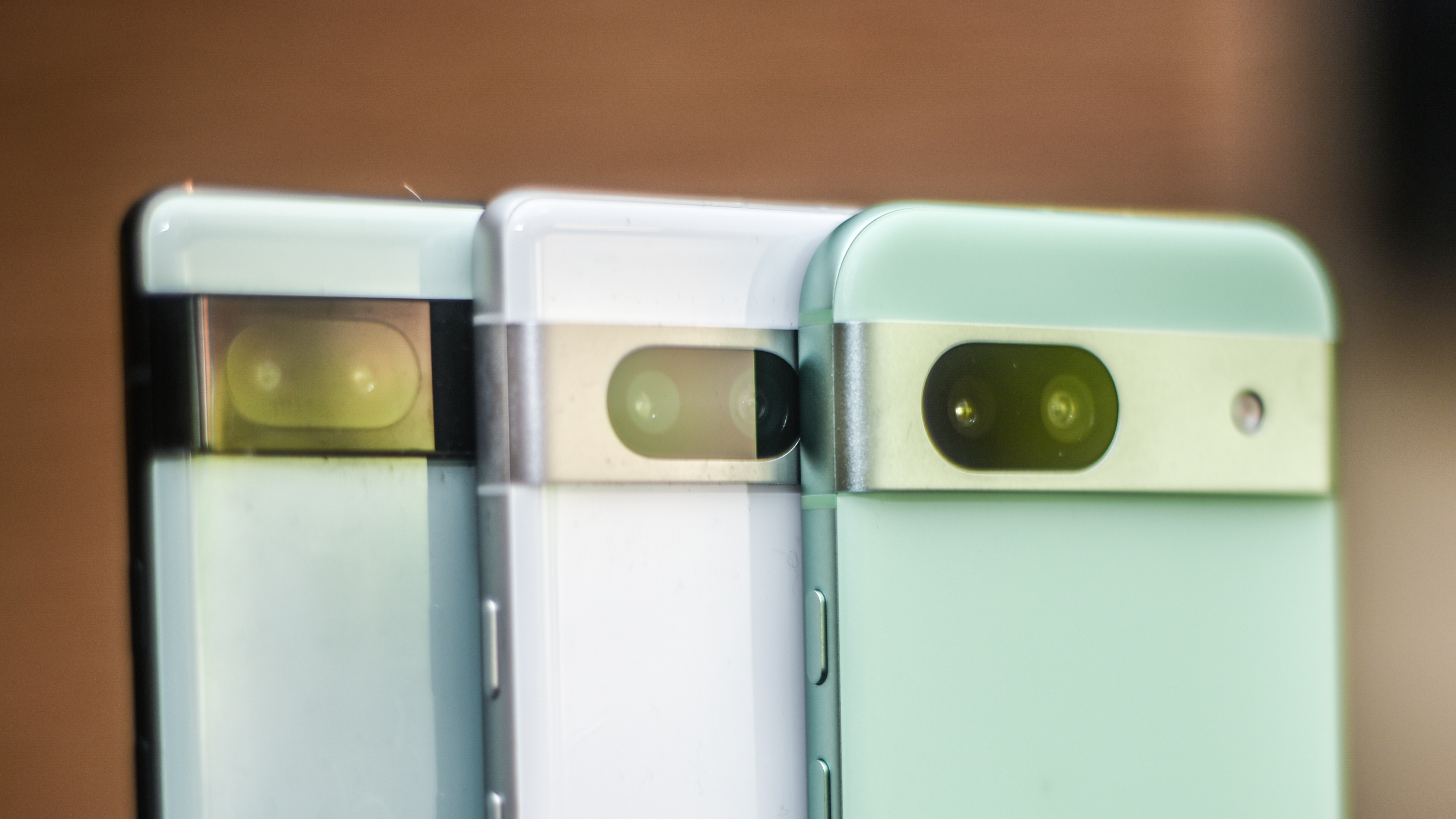 Google Pixel 8a in front of Pixel 7a in white and Pixel 6a in two-tone green and yellowish green