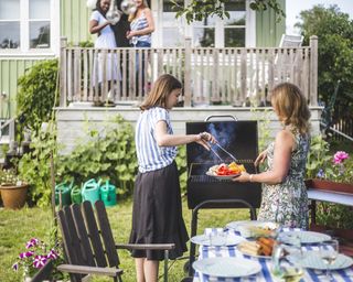 Mother and daughter preparing food on barbecue in backyard party