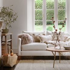 neutral living room with a cream sofa covered in cushions, and a wooden coffee table in front of it