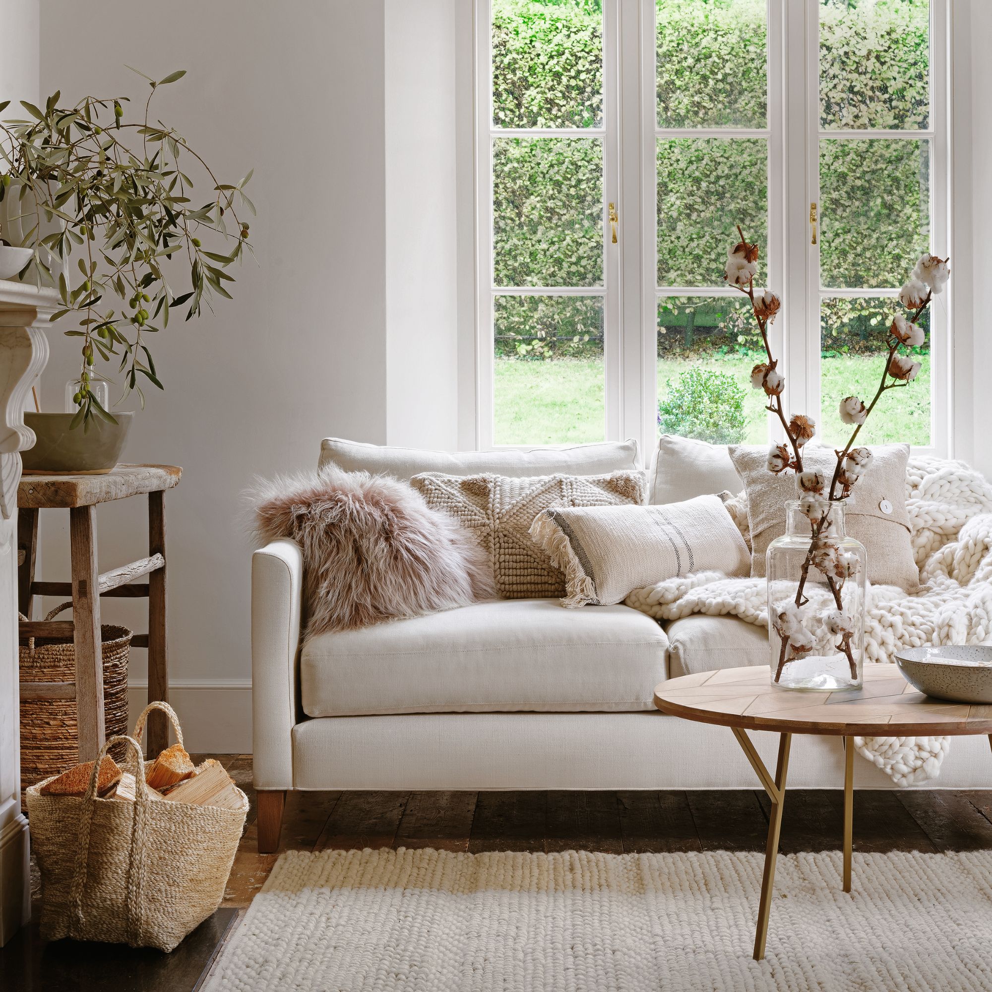 neutral living room with a cream sofa covered in cushions, and a wooden coffee table in front of it