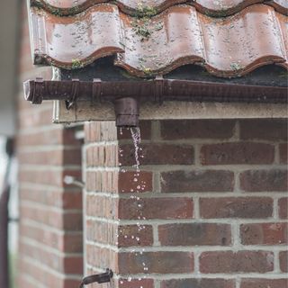 Brown broken gutter on a red bricked house with water coming out of it