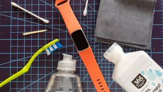A Fitbit Charge 6 shown next to cleaning tools including a toothbrush and rubbing alcohol.