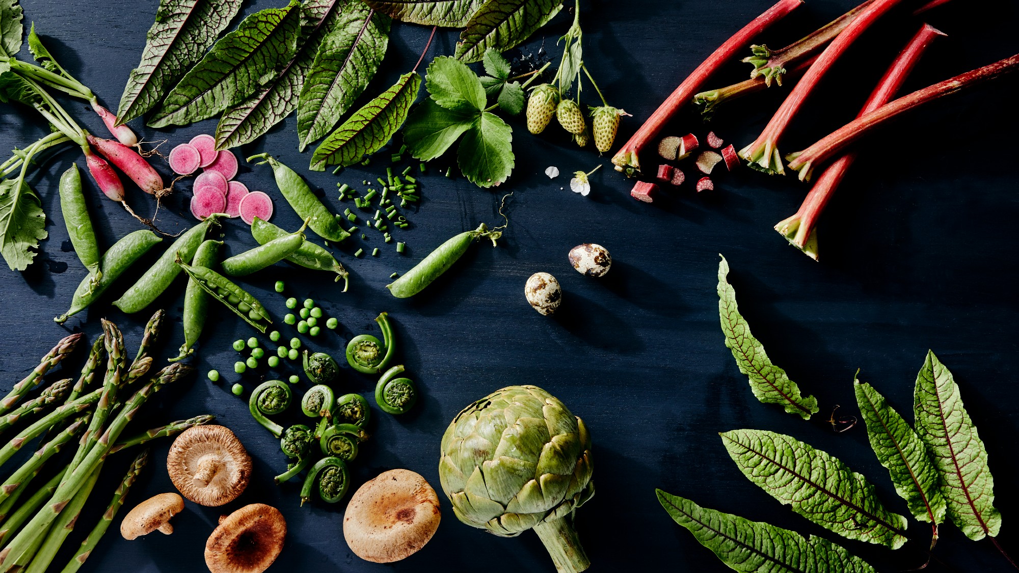 Overhead view of fresh spring vegetables sitting on a black background