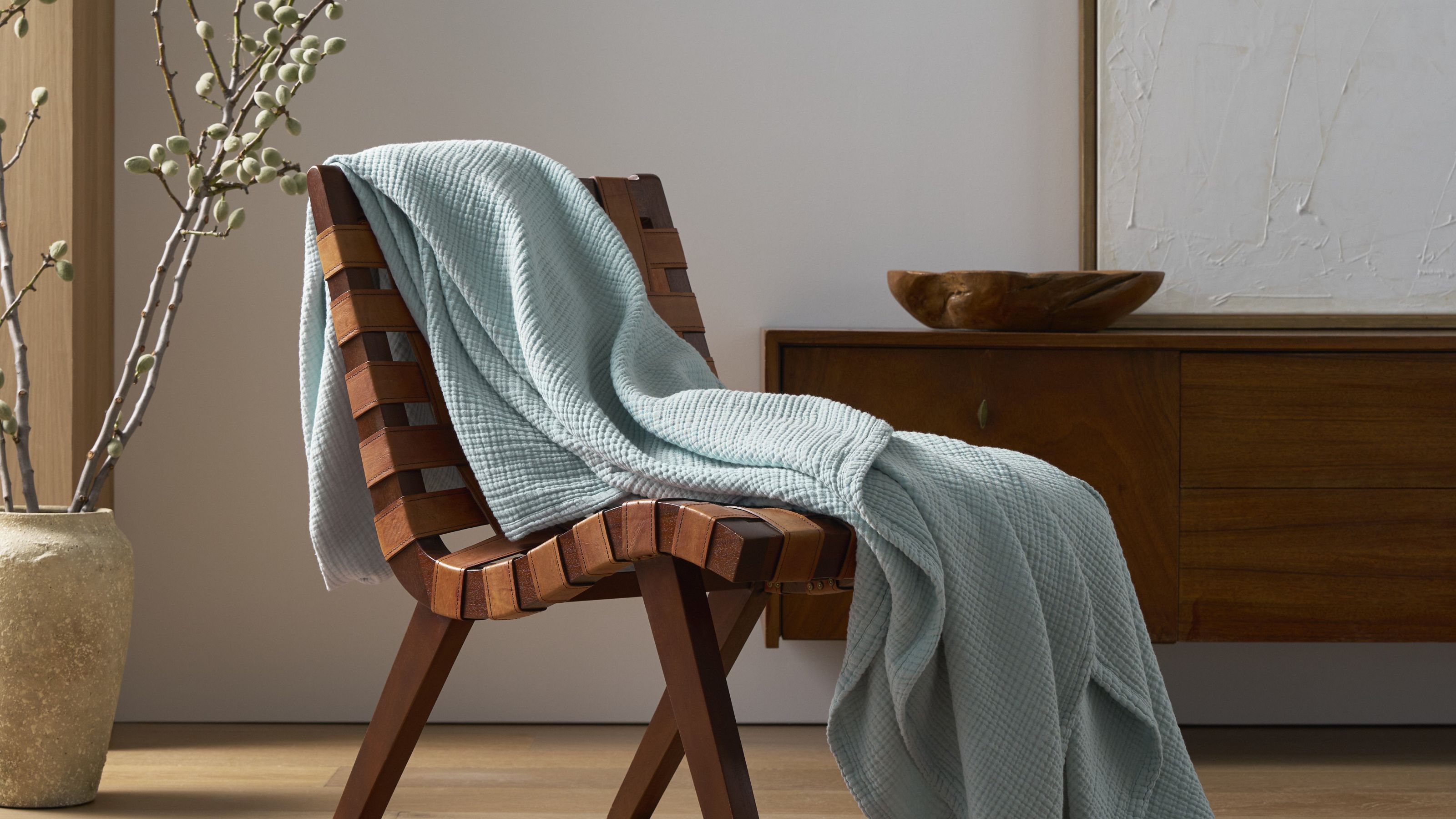 Cozy Earth Cotton Gauze Blanket in Tide draped over a woven chair in a contemporary living room