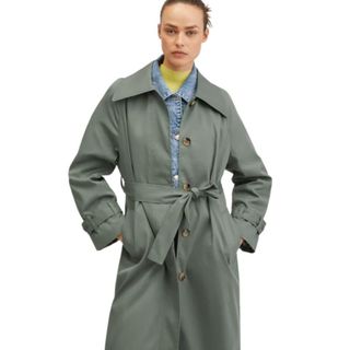 Model wearing khaki hued single breasted trench coat with belt