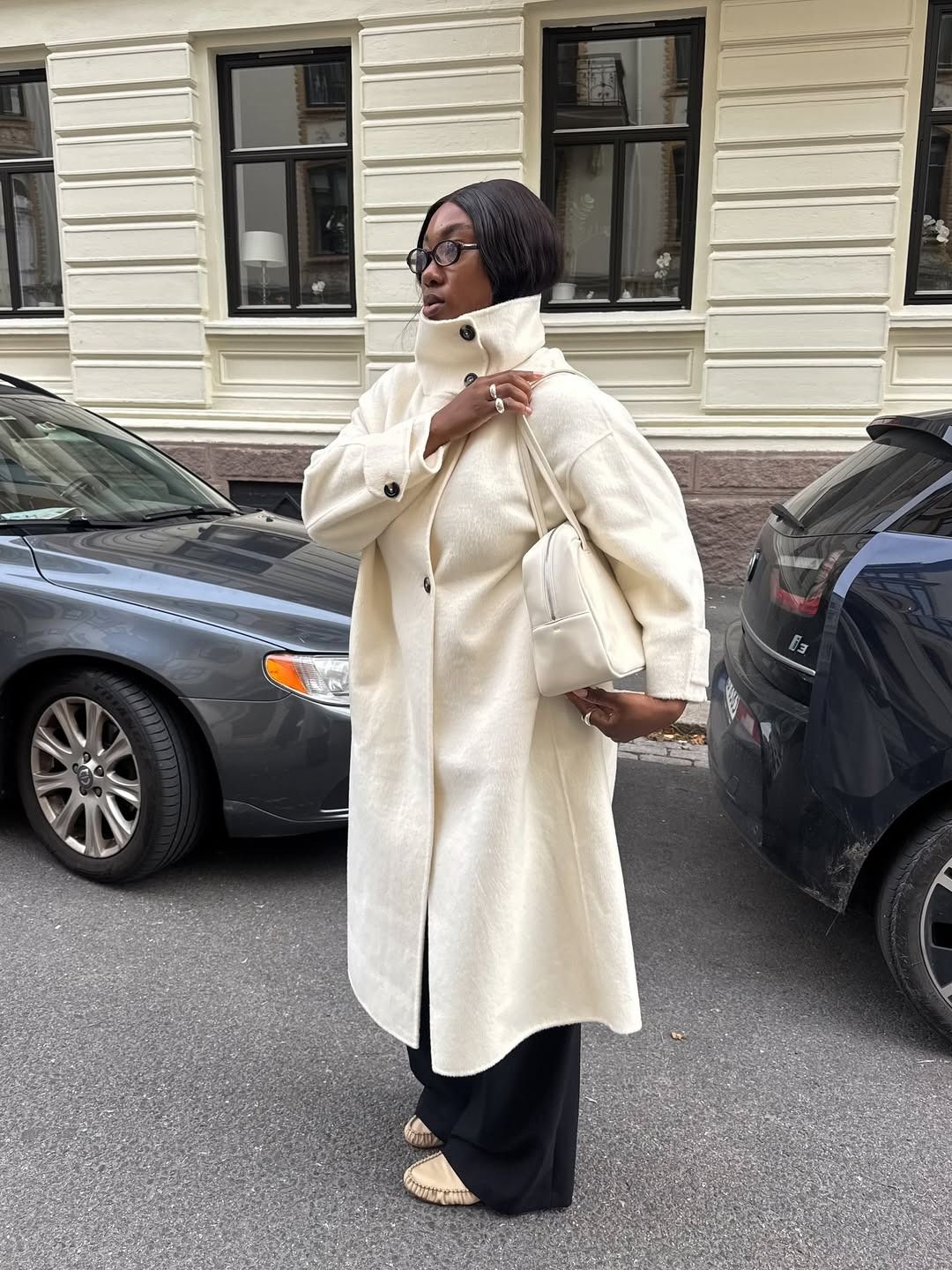 Influencer @nnennaechem wears a cream funnel neck coat with black trousers and leather loafers.