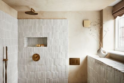 A bathroom with white zellige tiles and gold plumbing fixtures